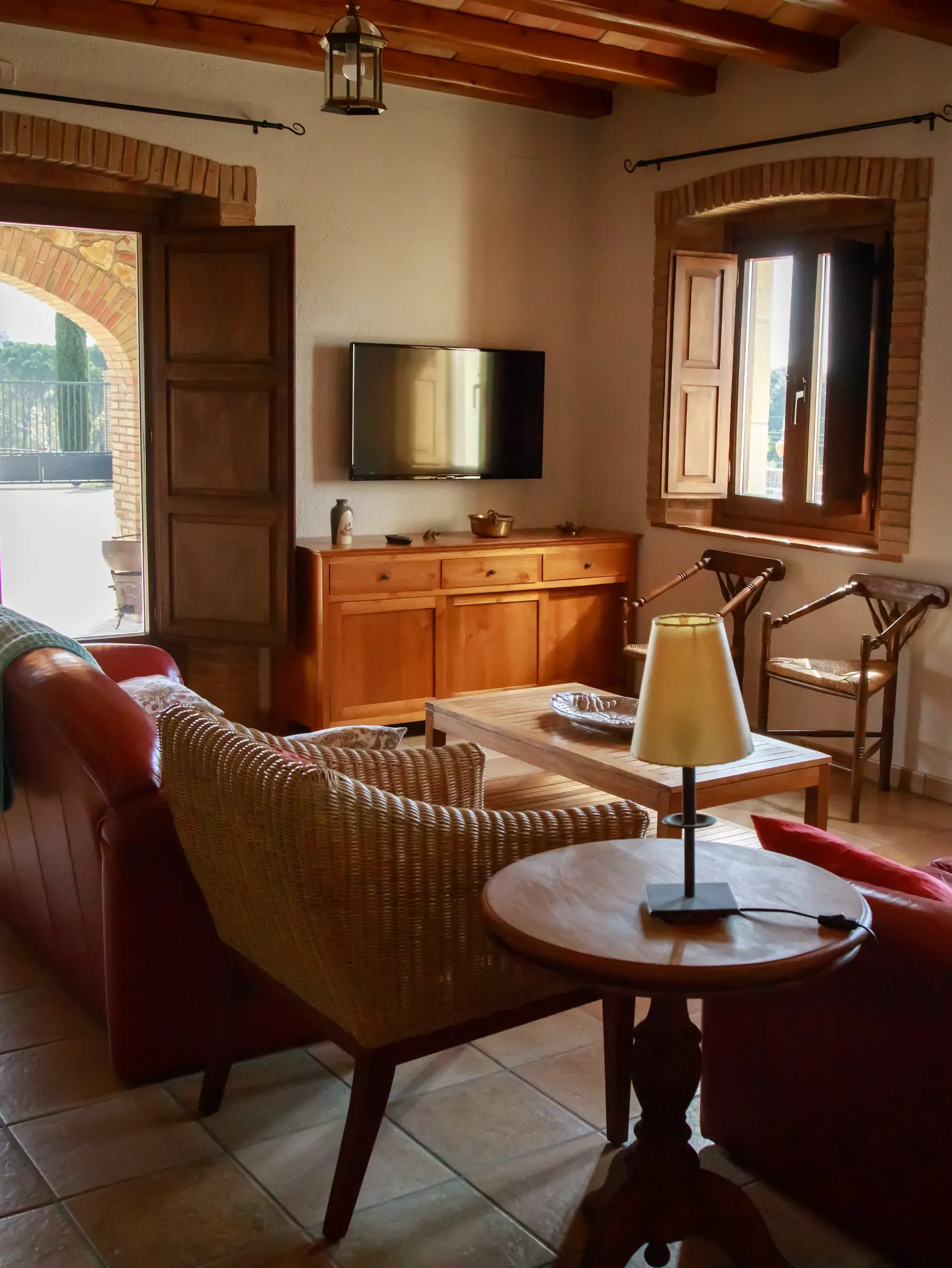 Una sala de estar luminosa con vigas de madera, azulejos de terracota, asientos de mimbre y cuero, una mesa de café y un televisor de pantalla plana.